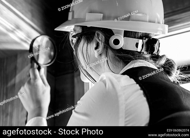 close up on woman inspector using a magnifying glass during air inspection, looking for molds or fungi on the wooden window edge. black and white