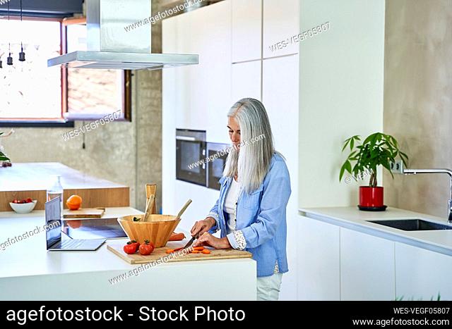 Mature woman cutting carrots on kitchen counter
