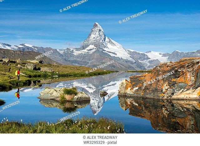 A walker hiking in the Alps takes in the view of the Matterhorn reflected in Stellisee lake at dawn, Swiss Alps, Switzerland, Europe