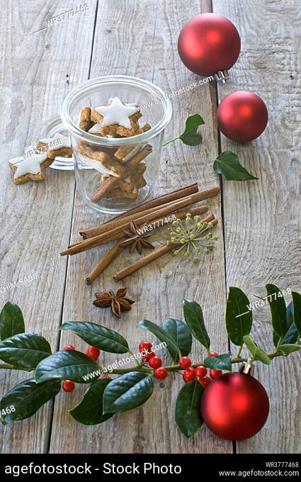Star-shaped cinnamon biscuits in a glass with cinnamon sticks, anise, red christmas baubles and a branch