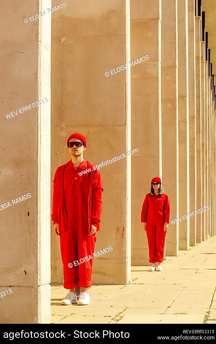 Young couple wearing red overalls and hats standing in a row