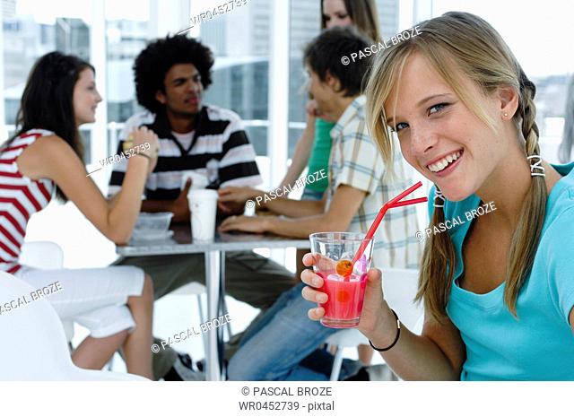 Portrait of a young woman holding a glass of juice in a restaurant with her friends sitting in the background