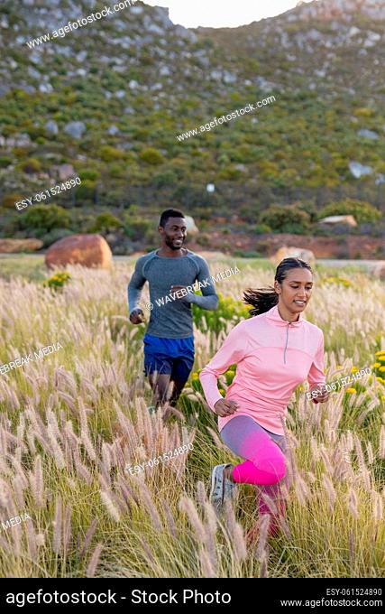 Fit african american couple in sportswear running through tall grass