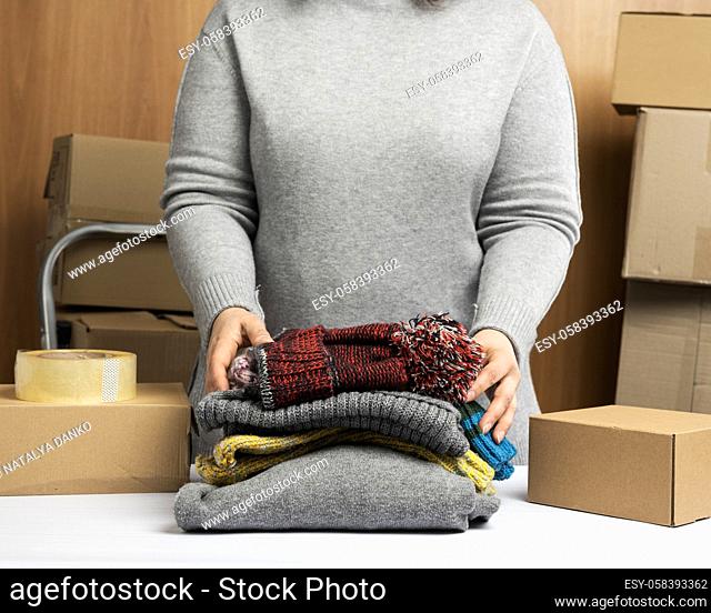 woman in a gray sweater collects clothes in a box, concept of assistance and volunteering, moving. Selling unnecessary things