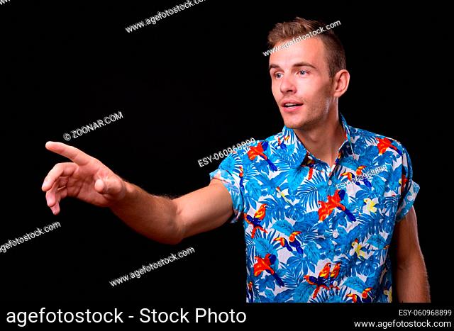 Studio shot of young handsome tourist man with blond hair ready for vacation against black background