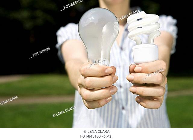 A young woman holding out a regular light bulb and an energy saving light bulb