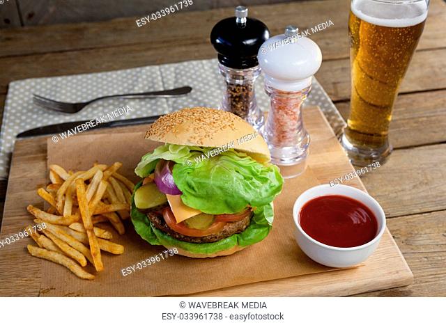 Hamburger, french fries, tomato sauce and glass of beer on chopping board