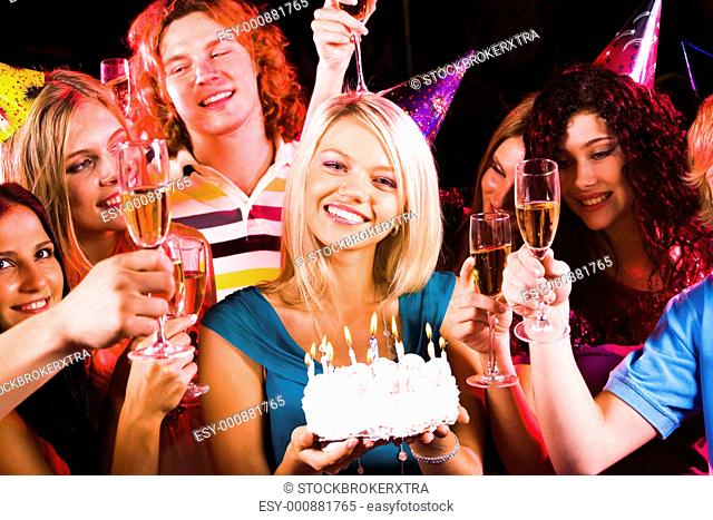 Portrait of joyful girl holding birthday cake surrounded by friends at party