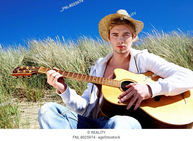 Portrait of a blonde young man playing guitar in the dunes