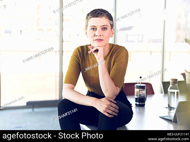 Portrait of businesswoman sitting on desk in office