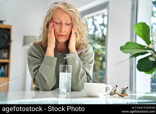 Stressed senior woman touching her face while drinking medicine