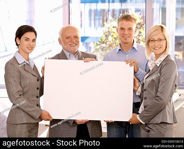 Businessteam standing in office, smiling, holding blank poster for copy space