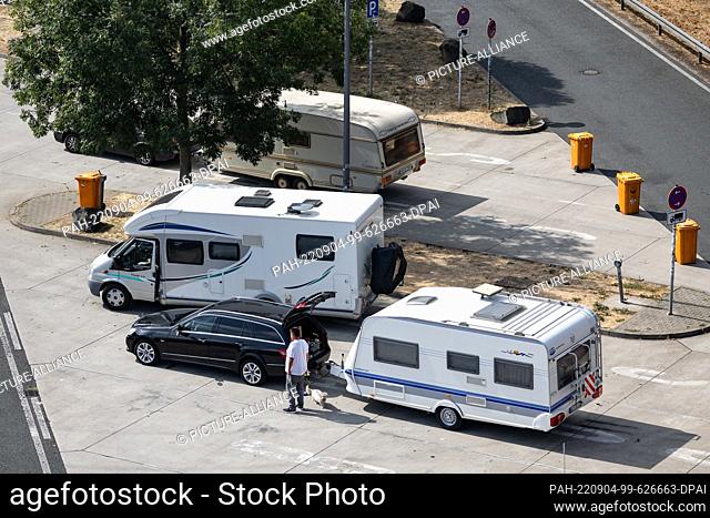 04 September 2022, Hessen, Eschborn: A person with a dog stands in front of a car with a caravan and next to two mobile homes at the Taunusblick rest stop