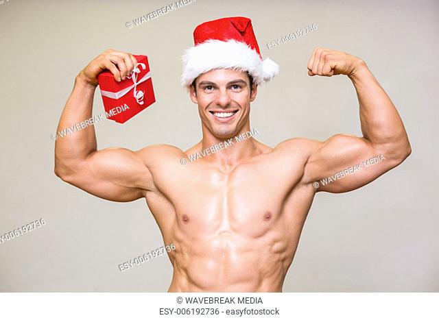 Portrait of shirtless macho man in santa hat holding gift