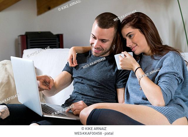 Young couple sitting on couch using laptop