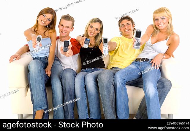 Small group of teenagers sitting on couch. Smiling and showing mobile phones. Looking at camera. White background, front view
