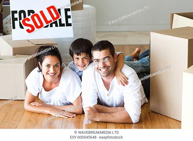 Happy family lying on the floor after buying new house with boxes