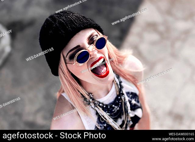 Portrait of screaming young woman wearing black wool cap and sunglasses