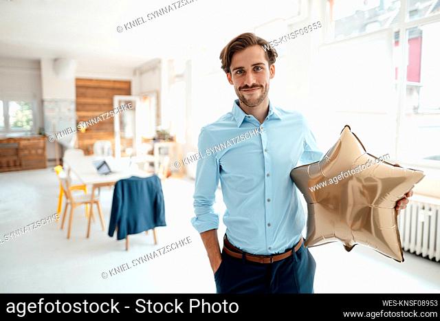 Smiling businessman holding golden star shape balloon in office