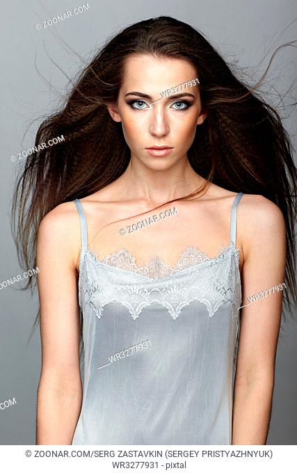 Beauty portrait of young woman. Brunette girl with long disheveled flying hair and day female makeup on gray background