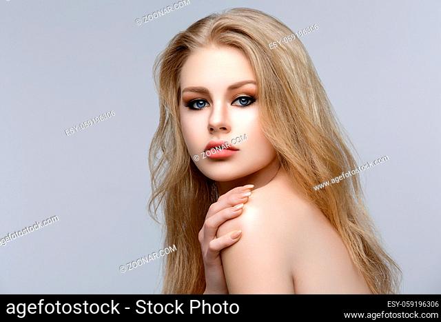 Closeup portrait of beautiful young woman with messy long blond hair and bright makeup. Beauty shot over grey background