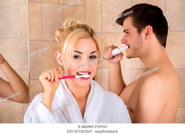Portrait Of Man And Woman Brushing Teeth In Bathroom At Home