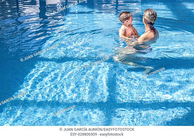 Mother playing with her baby at swimming pool indoor. Kids learn to swim during family vacation