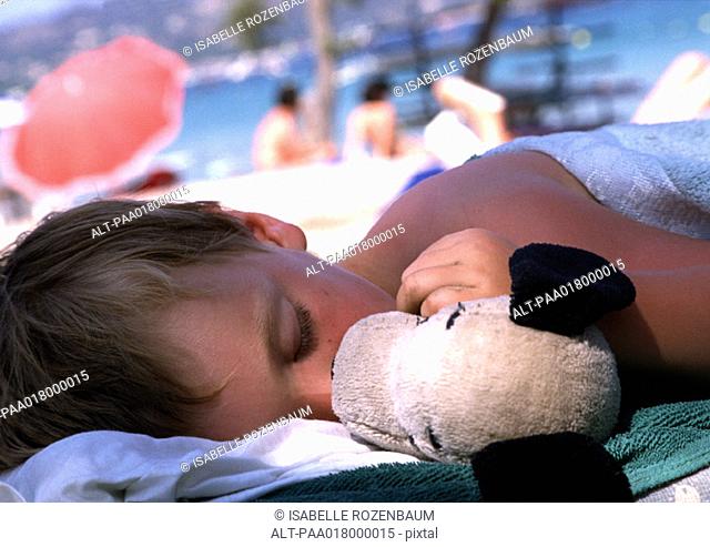 Child sleeping with doll at beach