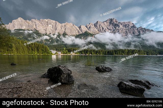 Rocks on the shore, Eibsee lake in front of Zugspitze massif with Zugspitze, low hanging clouds, Wetterstein range, near Grainau, Upper Bavaria, Bavaria