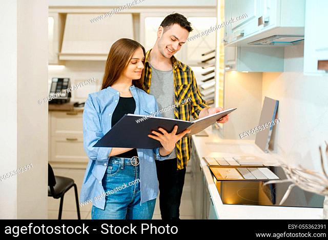 Family couple choosing kitchen garniture in furniture store showroom. Man and woman looking assortment in shop, husband and wife buys goods for modern home...