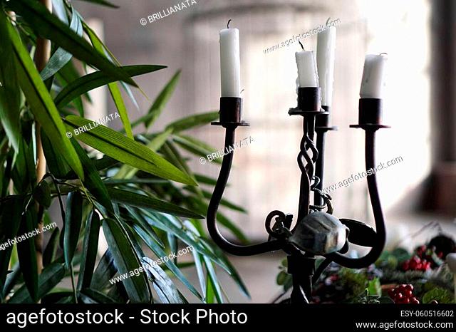 Forged metal candlestick with candles on blurred background with light from window