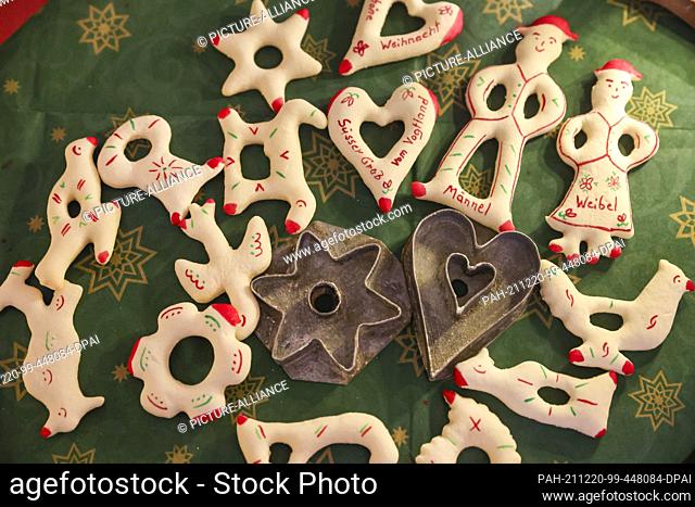 16 December 2021, Saxony, Werda: So-called Zuckermännle, historical Christmas biscuits from the Vogtland, lie on a table next to two historical cookie cutters