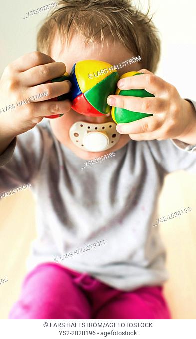 Little girl, 3 years old, having fun and hiding behind colorful balls