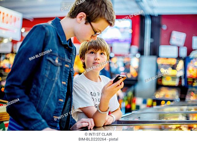 Caucasian brothers using cell phone in arcade