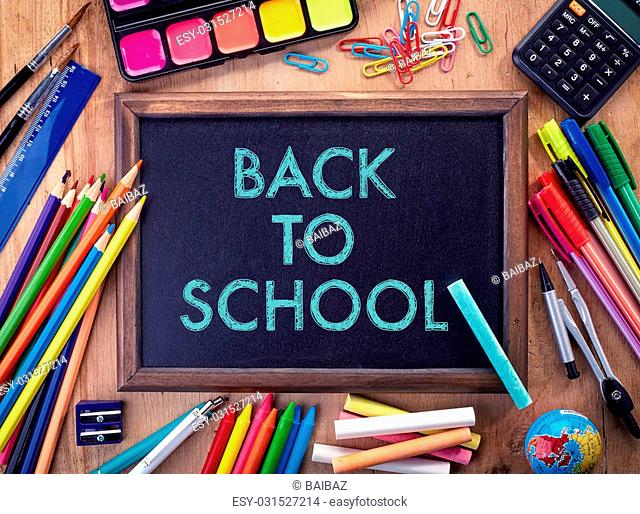 Chalkboard with back to school text and school office supplies on wooden background