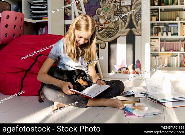 Girl reading book sitting with Miniature Pinscher dog at home