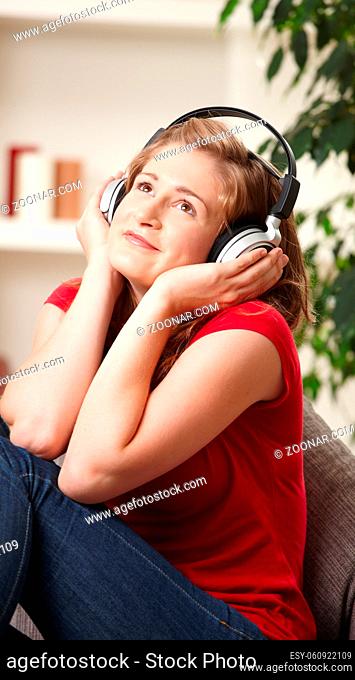 Happy teen girl listening to music on headphones sitting on couch at home smiling