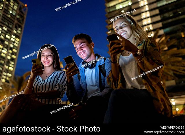 Happy young man and women surfing net through smart phones at night