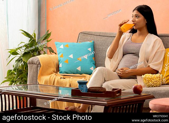 Pregnant woman drinking orange juice and relaxing at home