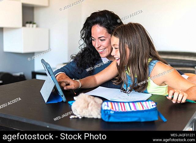 Mother guiding daughter learning on tablet PC at home