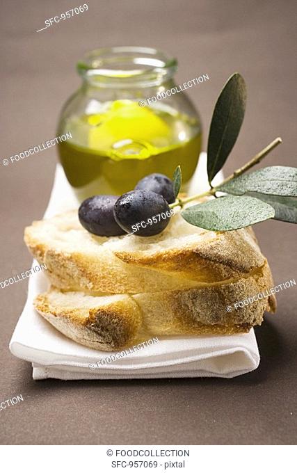 Olive sprig with black olives on white bread, olive oil behind