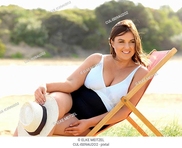 Woman in swimsuit sitting on beach chair, Point Impossible, Victoria, Australia