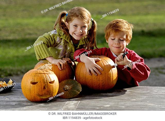 Two children carving pumpkins for Halloween decoration