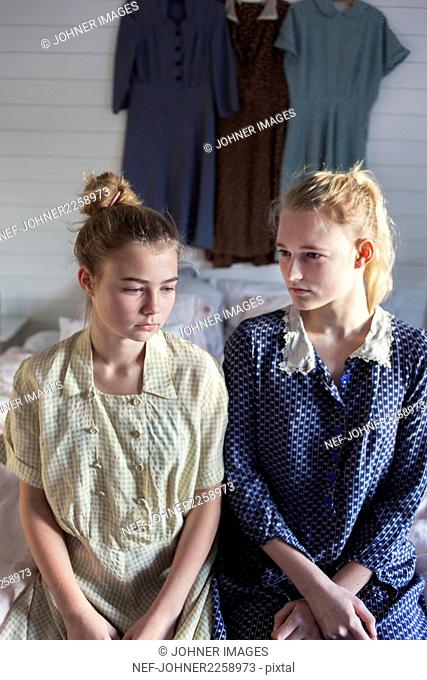 Two sad teenage girls sitting in bedroom