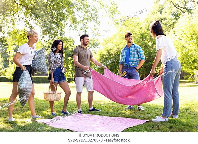 friends arranging place for picnic at summer park