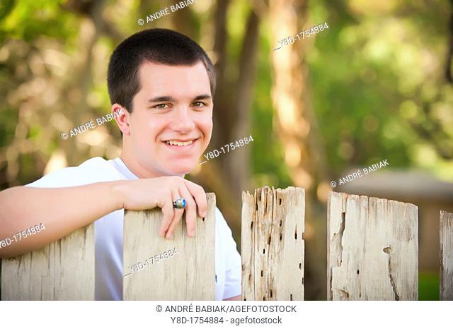 Portrait of male caucasian teenager, 17 years old, behind old wooden fence in Concan, TEXAS, USA