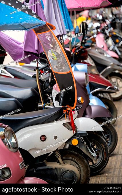 Yangshuo, China - August 2019 : Row of small motorbikes and scooters parked on a street in Yangshuo town, Guangxi Province
