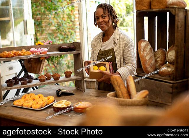 Portrait proud female baker boxing pastries in shop