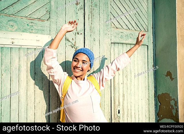 Cheerful beautiful woman with arms raised looking away in front of door during sunny day