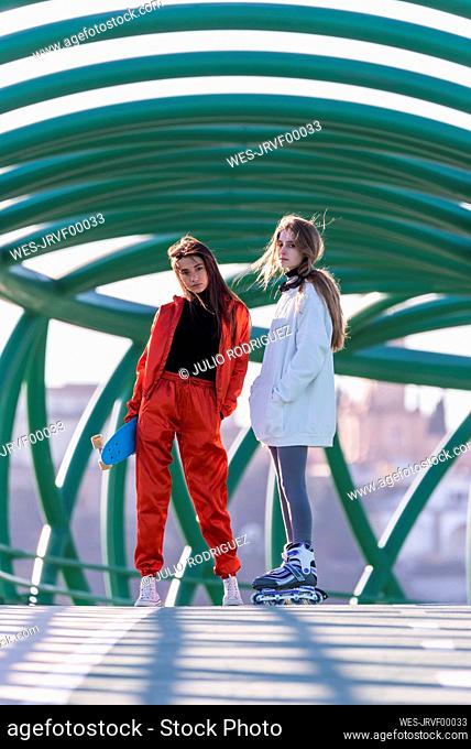 Teenage girl wearing roller skate standing with friend on bridge